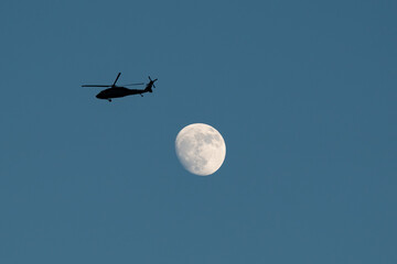 Striking night capture of a helicopter soaring in front of a glowing full moon, silhouetted against the dark sky—ideal for cinematic, aviation, or tactical storytelling projects.