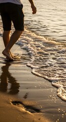 Close-up of feet walking through shallow water on a beach, foam and reflections, golden hour.