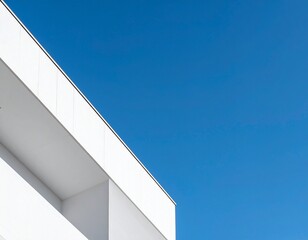 Sharp corner of modern white building against clear blue sky, minimal geometry.