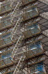 Zigzag metal fire escape casting shadows on urban building facade with blue window reflections