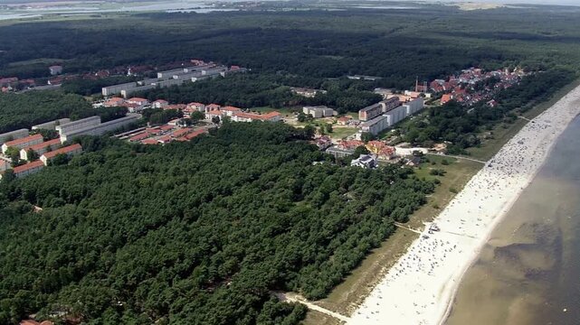 Aerial view of a beach with many people near a forest and buildings