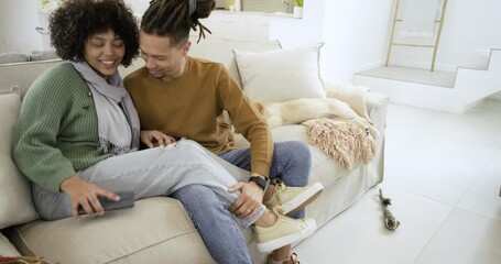 Couple leaning in sharing smartphone screen on light sofa, hugging after seeing message, surprised - Powered by Adobe