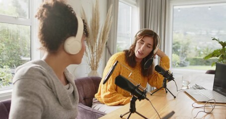 Diverse female coworkers at desk adjusting headphones toward mics using laptop cueing next segment