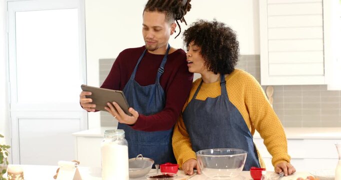 Cooking couple seeing recipe alert tablet, scrolling instructions and preparing batter at counter
