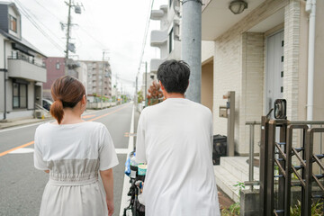 Fototapeta premium A man and woman are walking down a street. The man is wearing a white shirt and the woman is wearing a white dress. They are walking on a sidewalk next to a building