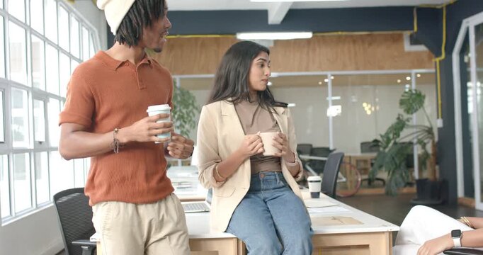 After arriving, Diverse coworkers holding mugs and cups while chatting over coffee break in office