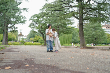 Fototapeta premium A couple holding a baby in a park. The baby is wearing a white shirt. The couple is walking on a path in the park