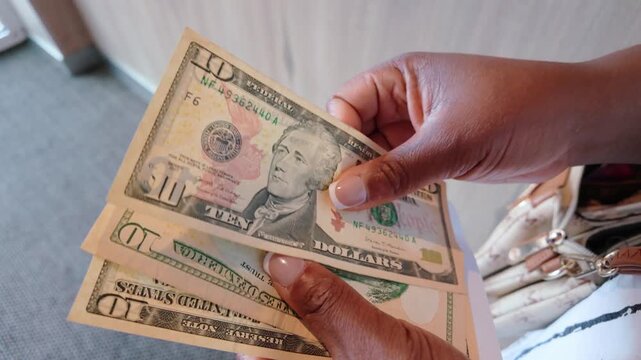 African American woman counting US dollar bills, focused on ten-dollar notes with detailed hands visible, highlighting financial activity