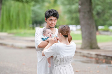 Fototapeta premium A man and woman are holding a baby in a park. The baby is wearing a blue shirt