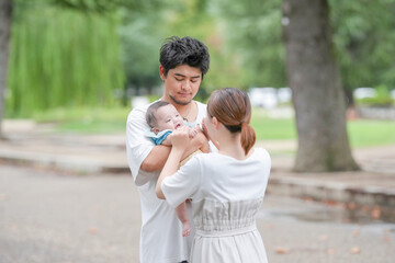 Fototapeta premium A man and a woman are holding a baby in a park. The baby is smiling and the family appears to be happy
