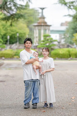 Fototapeta premium A man and woman holding a baby in front of a fountain. Scene is happy and loving