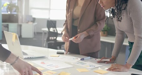 Diverse female colleagues pointing at Design note, reviewing charts on desk planning next steps - Powered by Adobe