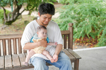 Fototapeta premium A man is holding a baby on a bench. The baby is wearing a blue shirt