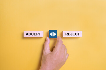 Male hand holds a wooden cube with arrow icon between the options of accept or reject