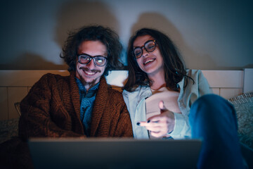 Couple watching movie on laptop at night in bed relaxing together streaming content digital lifestyle home entertainment cozy mood happy relationship millennial love.