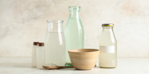 Different bottles of rice water and grains on light background