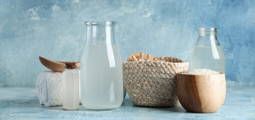 Bottles of rice water, grains, massage brush and clean towel on color background