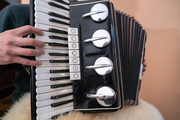 hands playing an old black accordion with piano keys, buttons, and extended red bellows