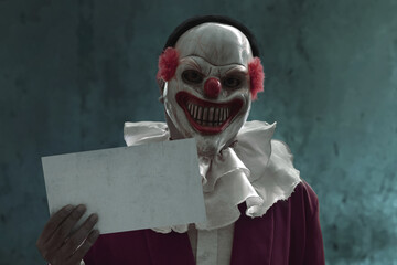Man wearing scary clown mask holding empty blank sign board, Halloween theme