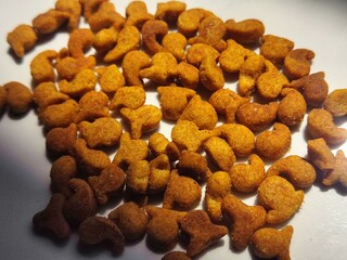 Cat food in the form of small dry grains resembling fish, golden brown in color, arranged randomly on a white surface