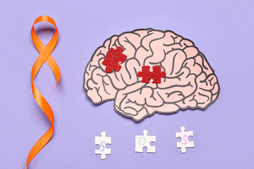 Paper brain with puzzle pieces and orange ribbon on lilac background. Multiple Sclerosis Awareness Month