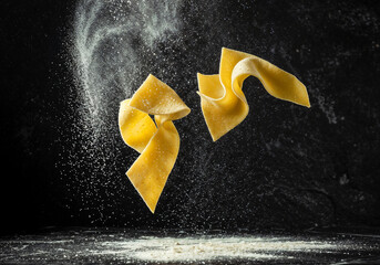 Fresh pasta sheets falling are surrounded by flour against dark backdrop showcasing culinary arts