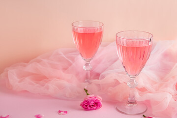 Glasses of tasty pink wine with beautiful rose and petals on color background