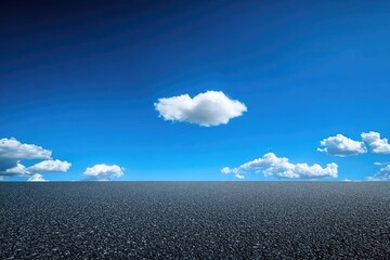 Open asphalt road stretches to a vibrant blue sky dotted with puffy white clouds