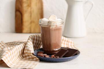Glass of sweet chocolate milk with marshmallows and cocoa beans on white background