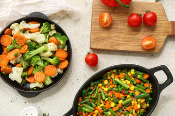 Frying pans with tasty roasted vegetables on white grunge background