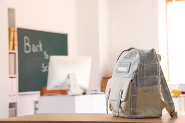 Fototapeta premium School backpack on wooden desk with blurred classroom background, back to school concept, education and learning