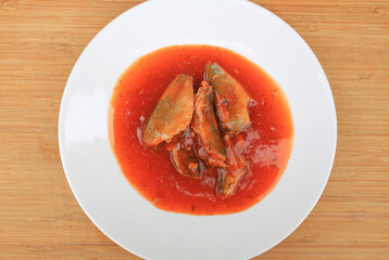 Juicy sardines or mackerel in rich tomato sauce, Beautifully served on white plate against wooden background, Top view.