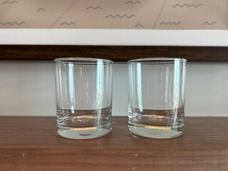 Two clean empty clear glass tumblers on a smooth textured wooden table surface