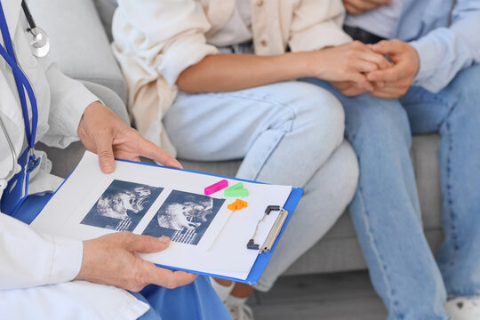 Female fertility doctor with sonogram image after IVF and couple sitting in clinic, closeup