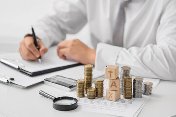 Cubes with word TAX and coins against businessman writing on table in office, closeup