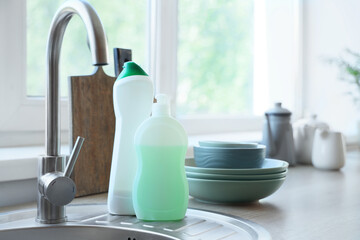 Bottles of detergents with clean dishes on sink in kitchen, closeup