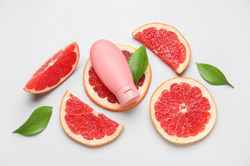 Composition with bottle of cosmetic product, green leaves and slices of grapefruit on white background, closeup
