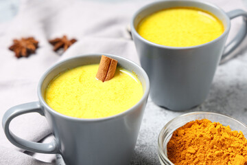 Cups of healthy turmeric drink on grey grunge background, closeup