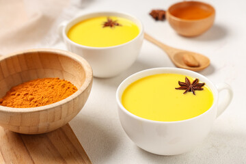 Composition with cups of healthy turmeric drink and ingredients on white background, closeup