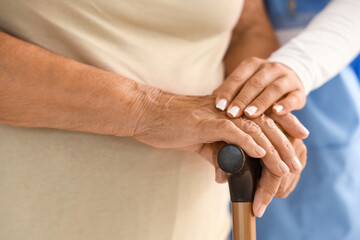 Female caregiver and senior woman with walking stick in bedroom, closeup