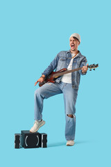 Naklejka premium Young man with speakers playing electric guitar on blue background