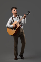 Young man with dreadlocks playing guitar on dark background