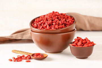 Bowls with dried goji berries on white wooden background, closeup