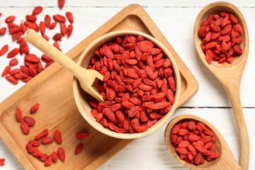 Bowl and spoons with dried goji berries on white wooden background, closeup