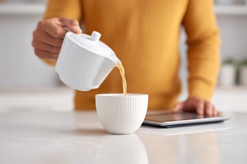 Pouring Hot Tea Into a White Cup While Using a Tablet at Home