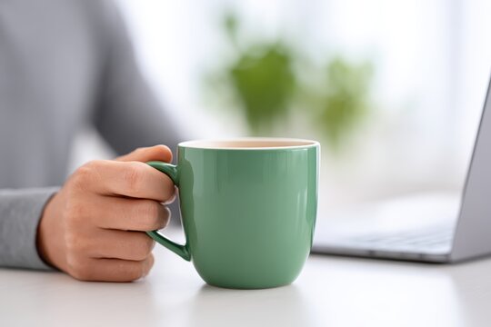 Hand Holding Green Mug Sitting on Table Near Laptop and Plant