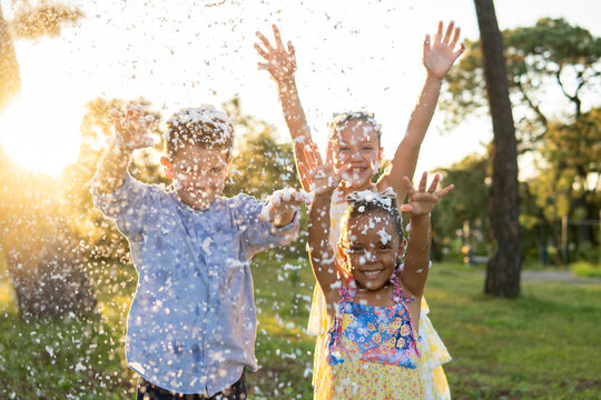 tres ni&ntilde;os felices jugando y disfrutando de su infancia e inocencia alegres y contentos en un parque al aire libre en un hermoso atardecer jugando con espuma 