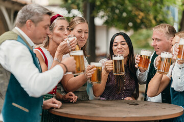 Cheerful group of men and women enjoy beer mugs in Bavarian beer garden celebrating friendship Oktoberfest leisure tradition and German culture
