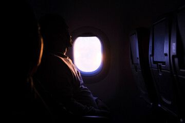 Passenger gazing through an airplane window as golden sunlight illuminates the cabin, creating a serene moment of reflection and travel ambiance during a quiet flight above the clouds.