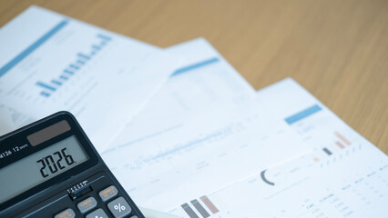 Calculator showing 2026 with financial reports and pen, symbolizing budget planning, investment...